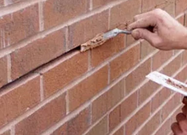 Mason raking out old mortar joints in a red brick wall